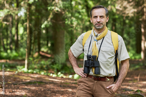 Waist up portrait of adult man as scout leader looking at camera outdoors in forest and smiling, copy space