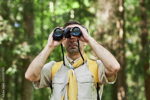 Waist up portrait of adult man as scout leader looking in binoculars in forest, copy space