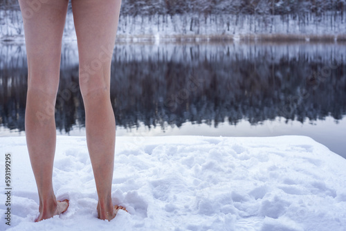 Kobieta stojąca zimą w negliżu na świeżym białym śniegu na pomoście nad jeziorem - zbliżenie na nogi