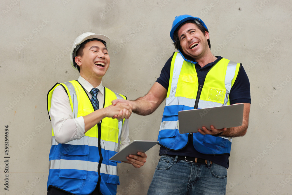 Two technician engineer man in protective uniform with hardhat standing and shaking hands celebrate successful together or completed deal commitment at industry warehouse manufacturing factory