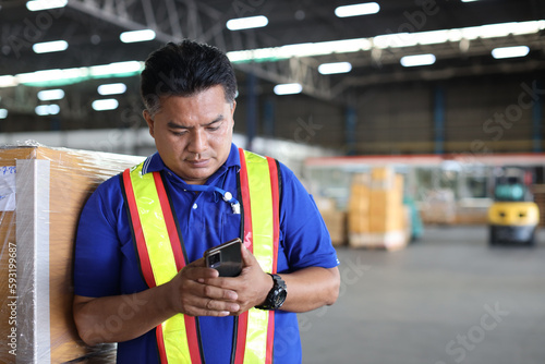 Warehouse workers man with hardhats and reflective jackets using smart mobile phone, walkie talkie radio controlling stock and inventory in retail warehouse logistics, distribution center