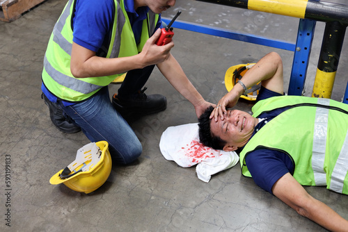 Safety colleagues team helping middle aged warehouse asian worker who had broken head accident and lying on the floor in warehouse while using walkie talkie radio. First aid training concept.