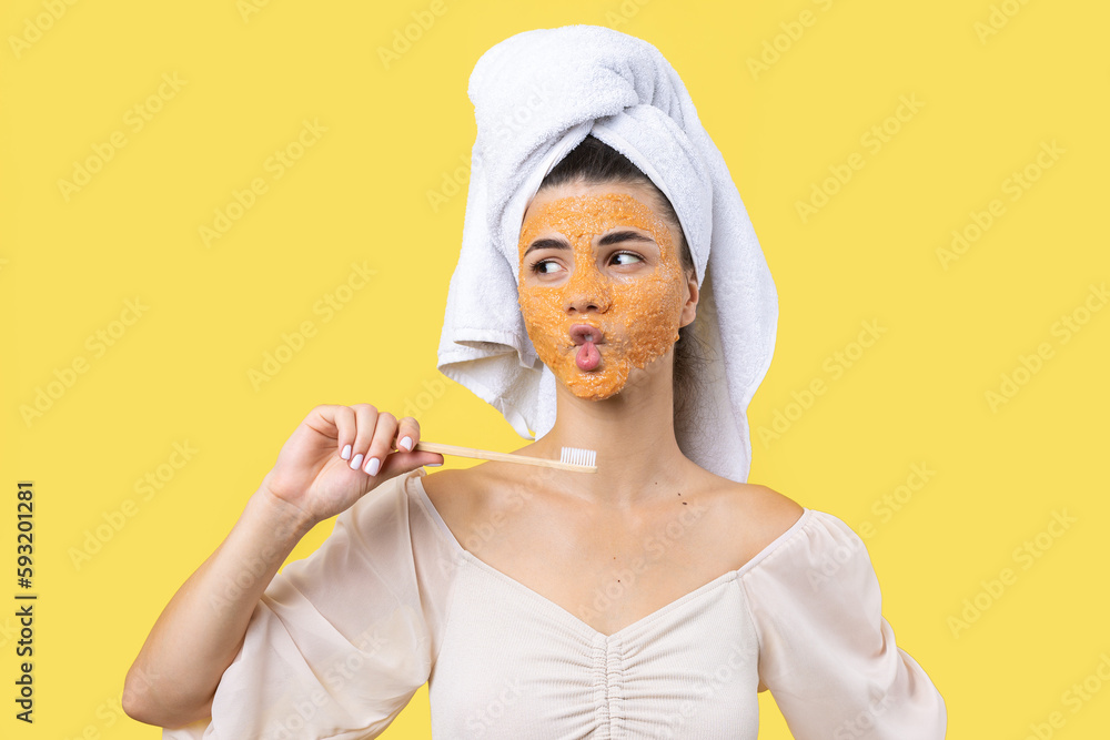 A cute young girl with a scrub mask on her face brushes her teeth against a yellow background. A cute young girl with a scrub mask on her face brushes her teeth against a yellow background.