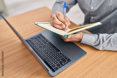 Young hispanic man writing on notebook at office