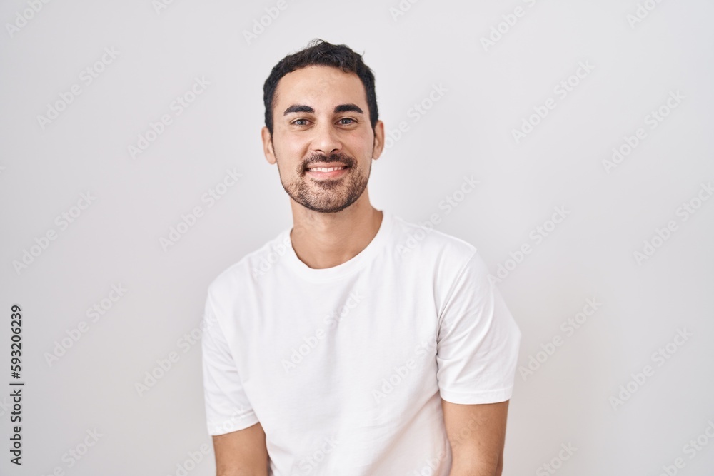 Handsome hispanic man standing over white background with hands together and crossed fingers smiling relaxed and cheerful. success and optimistic Handsome hispanic man standing over white background with hands together and crossed fingers smiling relaxed and cheerful. success and optimistic