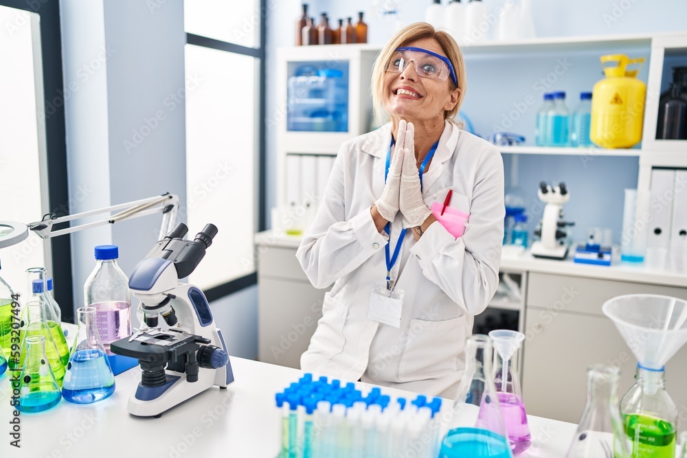 Middle age blonde woman working at scientist laboratory praying with hands together asking for forgiveness smiling confident. Middle age blonde woman working at scientist laboratory praying with hands together asking for forgiveness smiling confident.