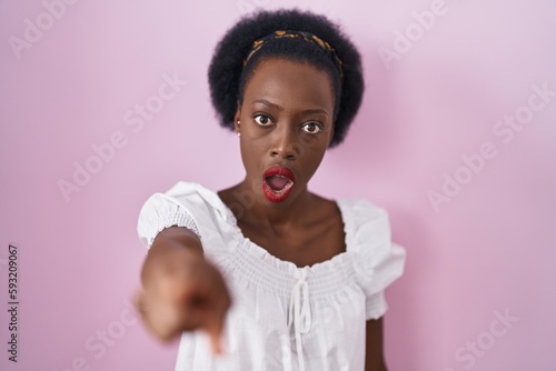African woman with curly hair standing over pink background pointing displeased and frustrated to the camera, angry and furious with you
