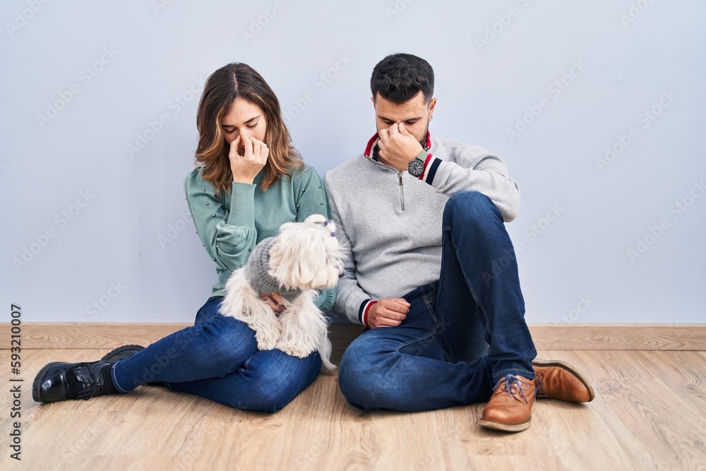 Young hispanic couple sitting on the floor with dog tired rubbing nose and eyes feeling fatigue and headache. stress and frustration concept. Young hispanic couple sitting on the floor with dog tired rubbing nose and eyes feeling fatigue and headache. stress and frustration concept.