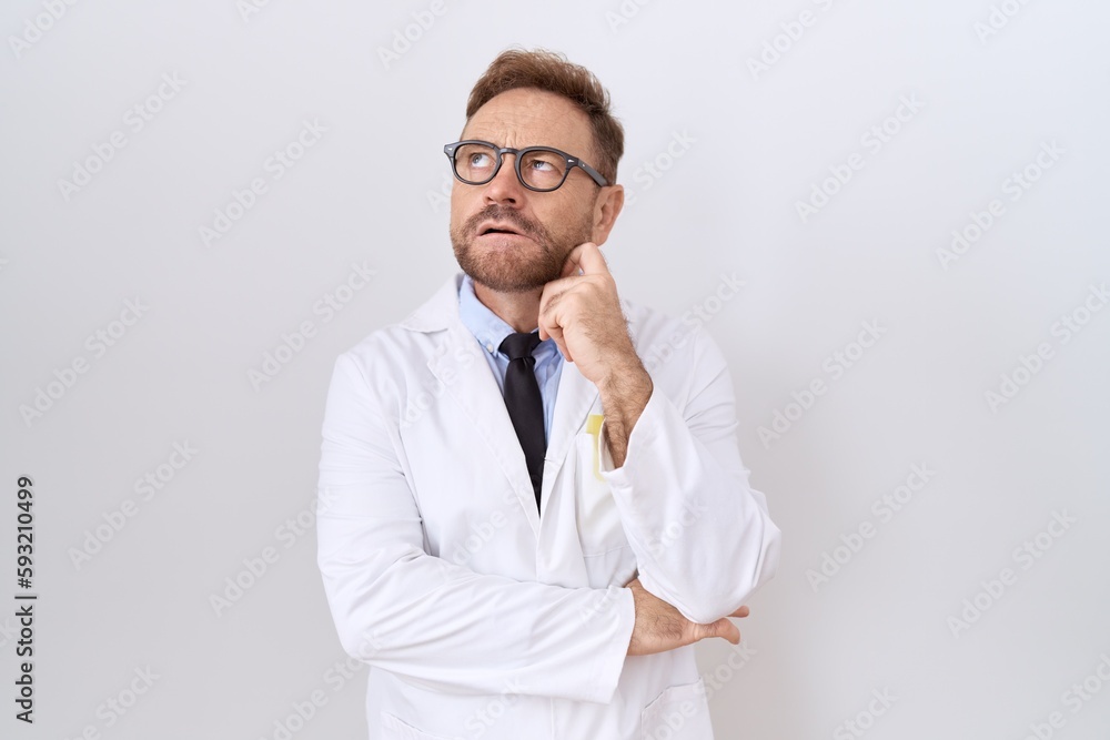Middle age doctor man with beard wearing white coat with hand on chin thinking about question, pensive expression. smiling with thoughtful face. doubt concept. Middle age doctor man with beard wearing white coat with hand on chin thinking about question, pensive expression. smiling with thoughtful face. doubt concept.