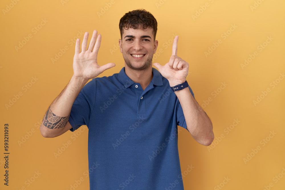Young hispanic man standing over yellow background showing and pointing up with fingers number seven while smiling confident and happy. Young hispanic man standing over yellow background showing and pointing up with fingers number seven while smiling confident and happy.