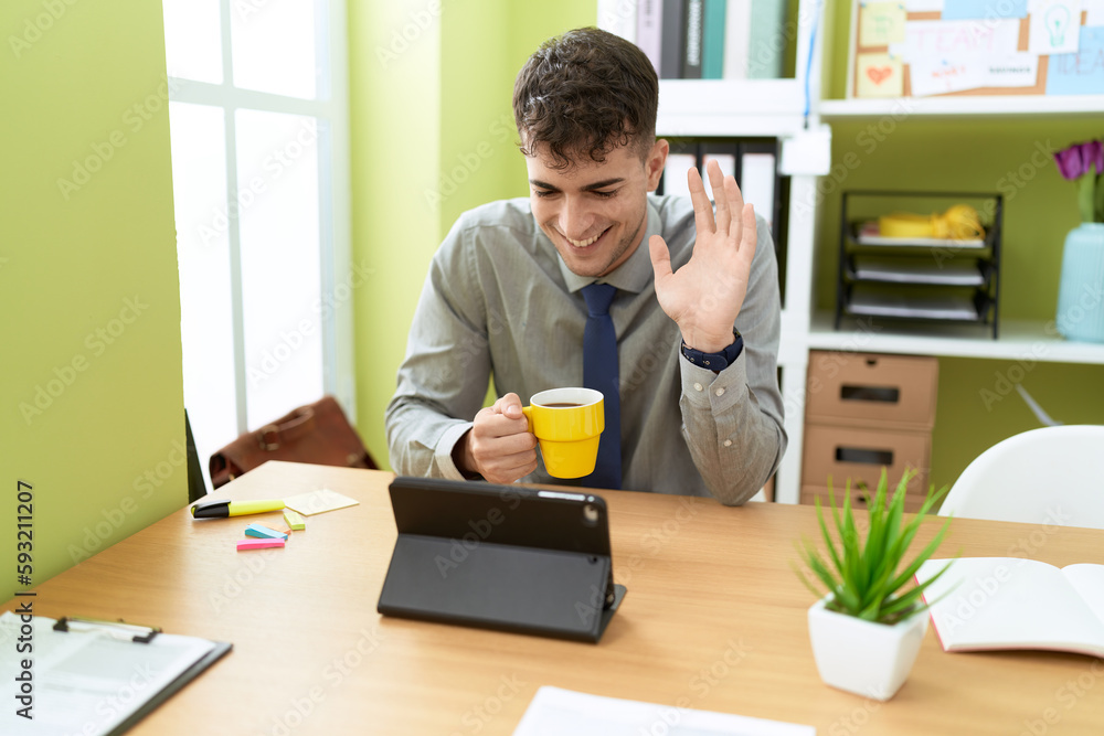 Young hispanic man business worker having video call drinking coffee at office