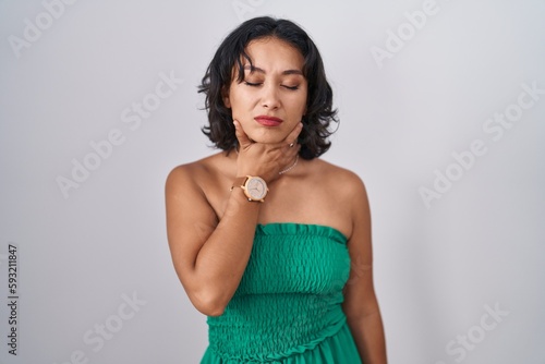 Young hispanic woman standing over isolated background touching painful neck, sore throat for flu, clod and infection