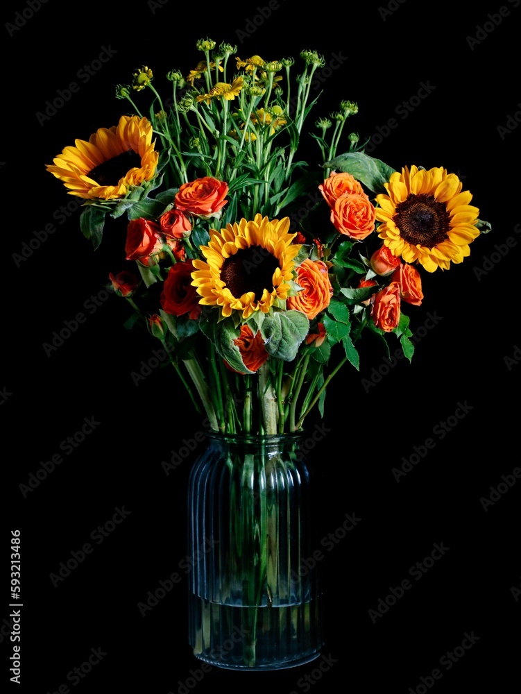 Fototapeta premium Vertical shot of a bouquet of sunflowers and roses in a vase isolated on a dark background