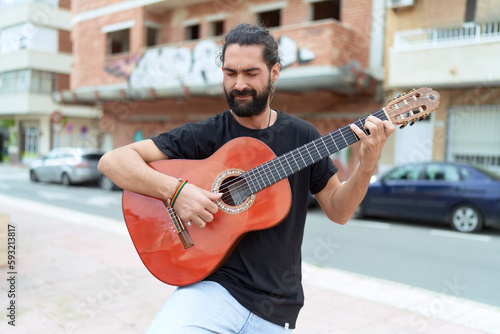 Young hispanic man musician playing classical guitar at street