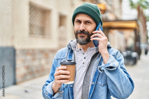 Young bald man talking on smartphone drinking coffee at street