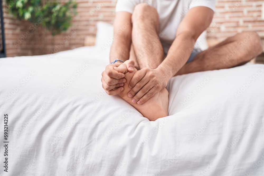 Young hispanic man suffering for feet pain sitting on bed at bedroom Young hispanic man suffering for feet pain sitting on bed at bedroom