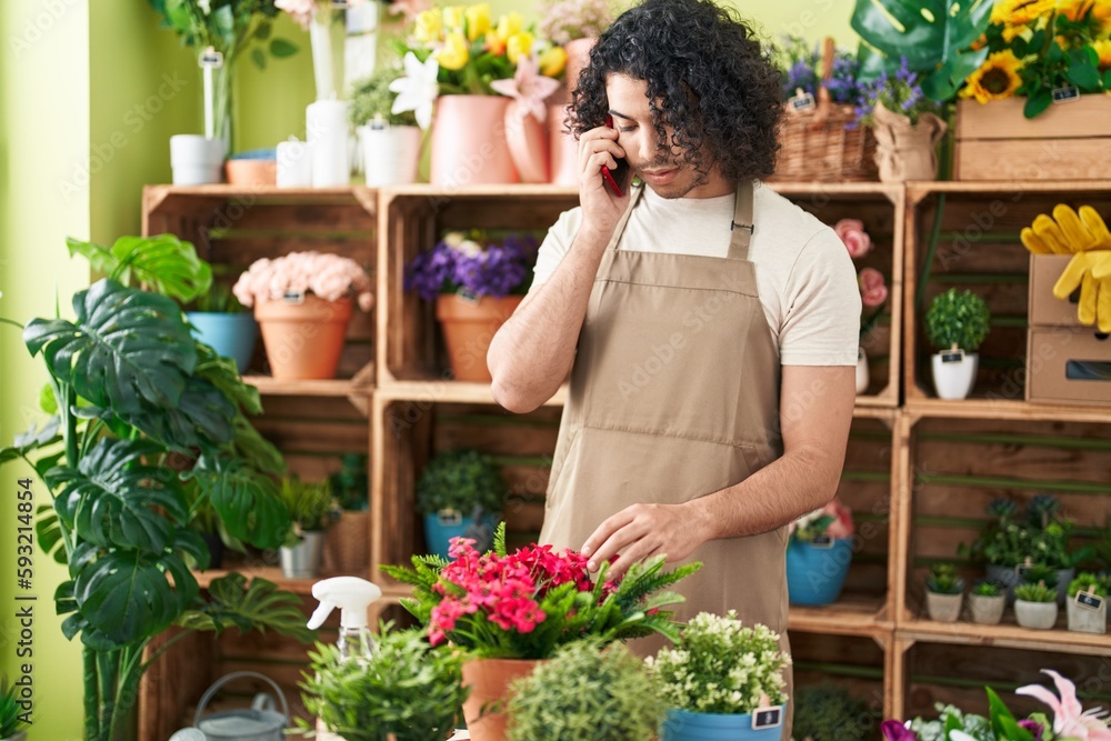 Young latin man florist talking on smartphone at flower shop