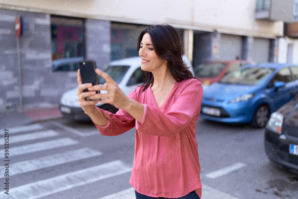 Fototapeta premium Middle age hispanic woman smiling confident making selfie by the smartphone at street