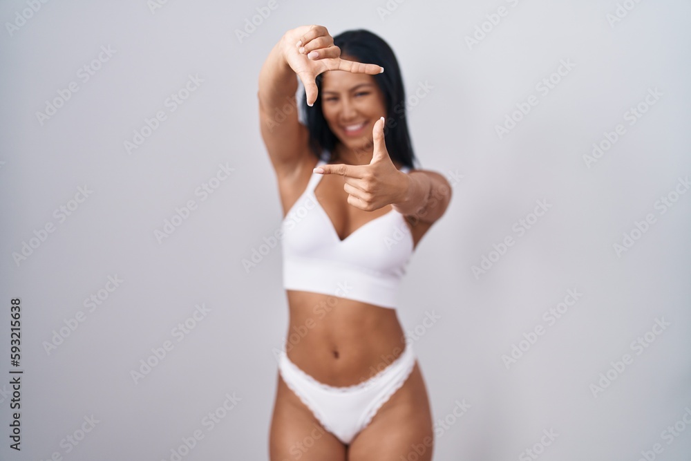 Hispanic woman wearing lingerie smiling making frame with hands and fingers with happy face. creativity and photography concept. Hispanic woman wearing lingerie smiling making frame with hands and fingers with happy face. creativity and photography concept.
