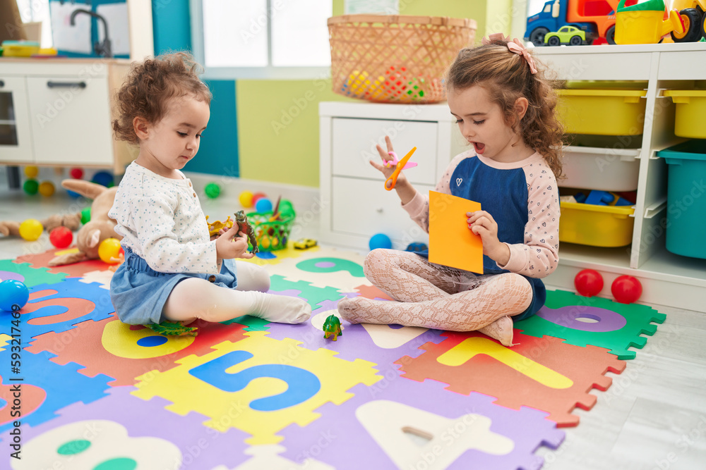 Naklejka premium Adorable girls student cutting paper playing with dinosaur toy at kindergarten