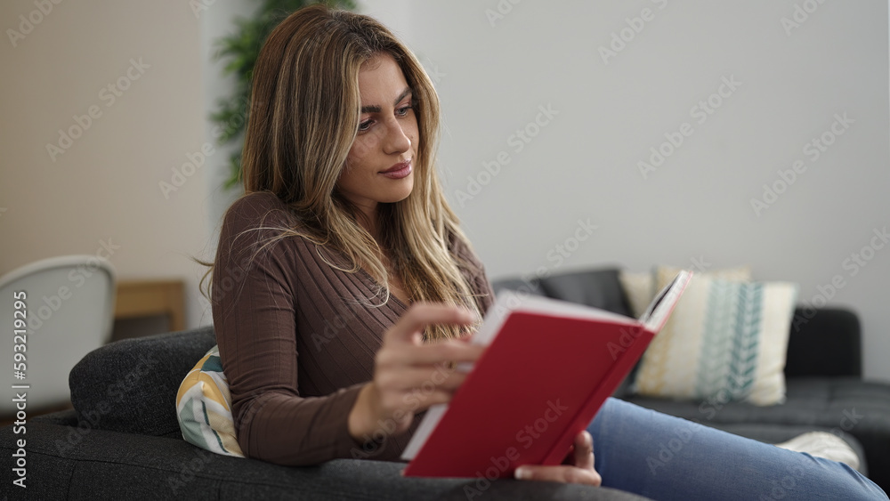 Young blonde woman reading book sitting on sofa at home Young blonde woman reading book sitting on sofa at home