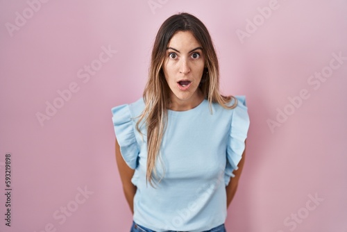 Young hispanic woman standing over pink background afraid and shocked with surprise expression, fear and excited face.