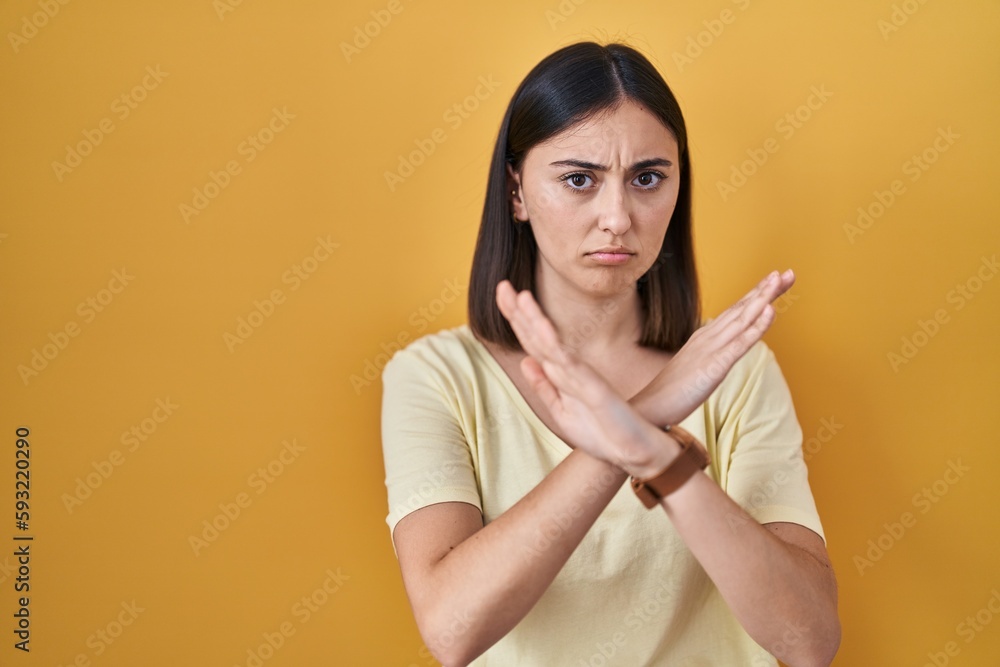 Obraz premium Hispanic girl wearing casual t shirt over yellow background rejection expression crossing arms doing negative sign, angry face