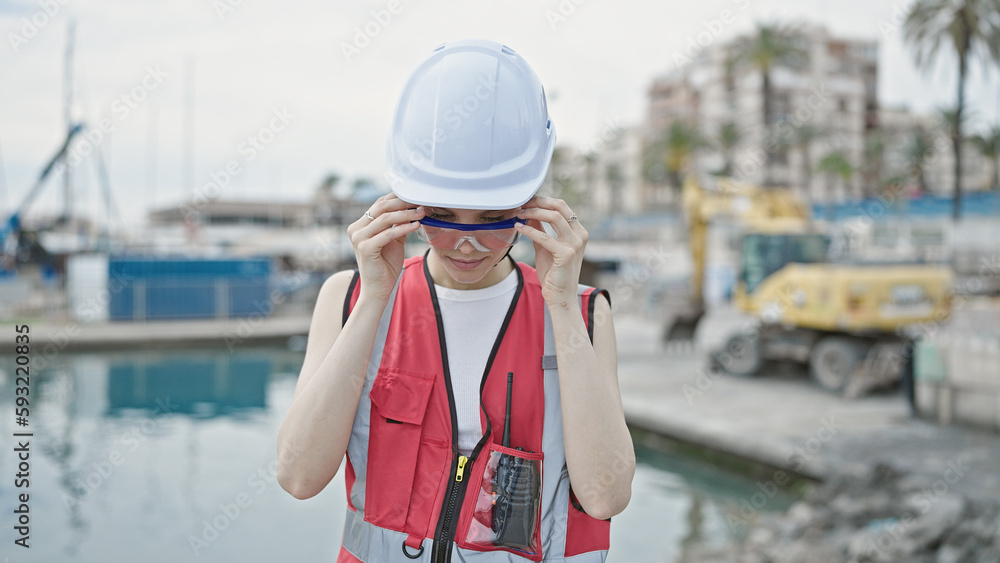 Obraz premium Young beautiful hispanic woman builder standing with serious expression wearing glasses at seaside