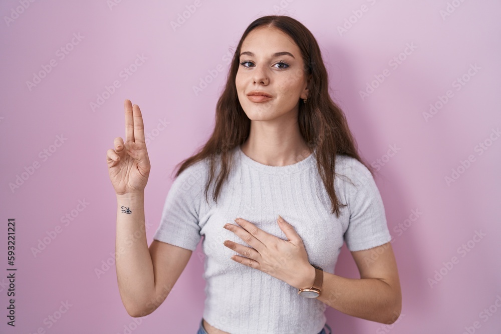 Young hispanic girl standing over pink background smiling swearing with hand on chest and fingers up, making a loyalty promise oath Young hispanic girl standing over pink background smiling swearing with hand on chest and fingers up, making a loyalty promise oath