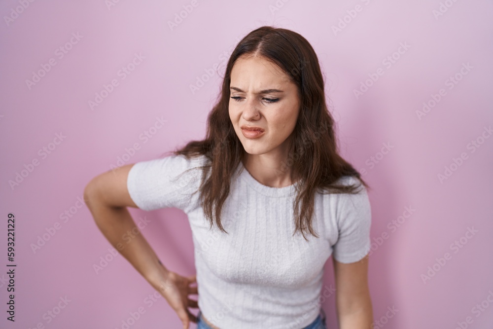 Young hispanic girl standing over pink background suffering of backache, touching back with hand, muscular pain Young hispanic girl standing over pink background suffering of backache, touching back with hand, muscular pain