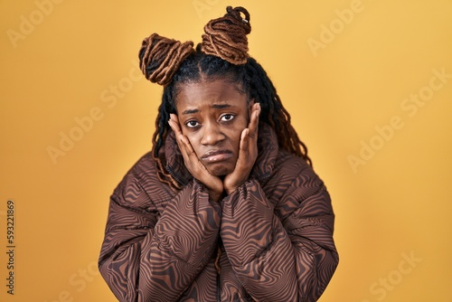 African woman with braided hair standing over yellow background tired hands covering face, depression and sadness, upset and irritated for problem © Krakenimages.com