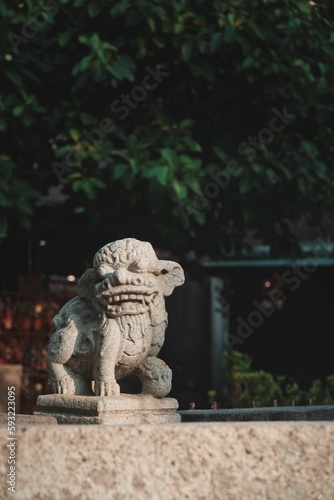 Vertical shot of a Chinese lion sculpture in the park with trees in the background © Hys/Wirestock Creators