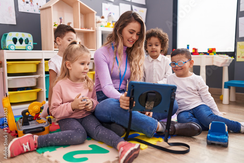 Woman and group of kids having lesson using touchpad at kindergarten