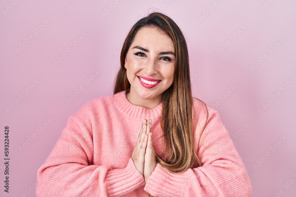 Young hispanic woman standing over pink background praying with hands together asking for forgiveness smiling confident. Young hispanic woman standing over pink background praying with hands together asking for forgiveness smiling confident.