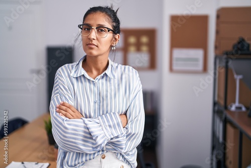 Young beautiful hispanic woman business worker standing with arms crossed gesture at office