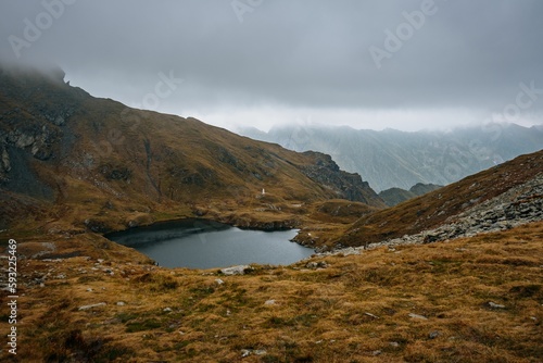 Beautiful small Capra Lake in Romania surrounded by the big mountains under the gloomy sky