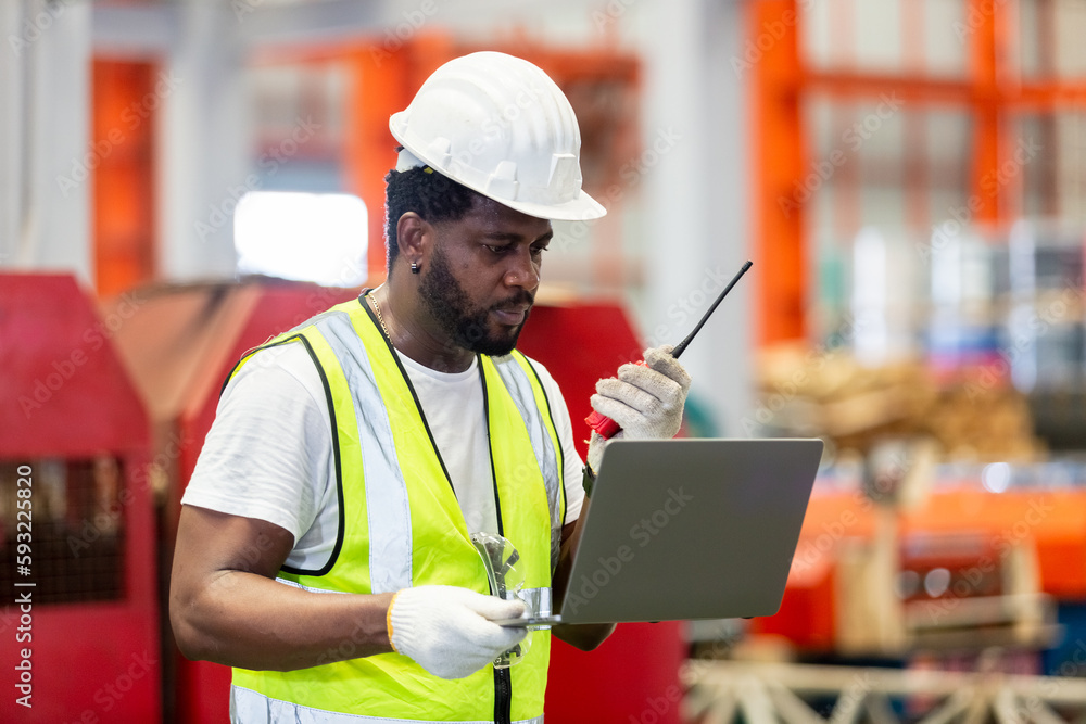 Fototapeta premium African American engineer worker male holding walkie talkie using laptop working in manufacturing factory. technician metalwork automated mechanic energy project.