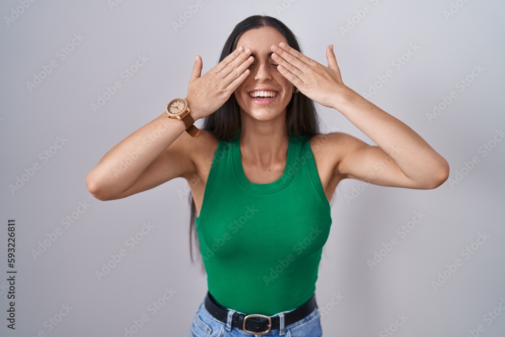 Young woman standing over isolated background covering eyes with hands smiling cheerful and funny. blind concept. Young woman standing over isolated background covering eyes with hands smiling cheerful and funny. blind concept.
