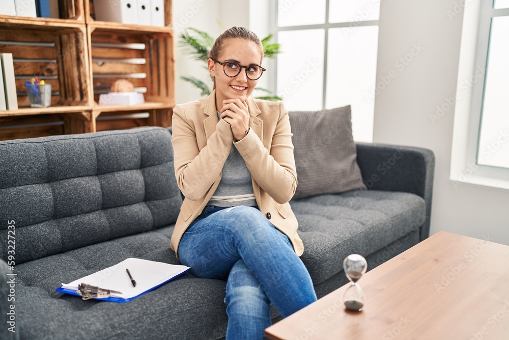 Young woman working at consultation office laughing nervous and excited with hands on chin looking to the side