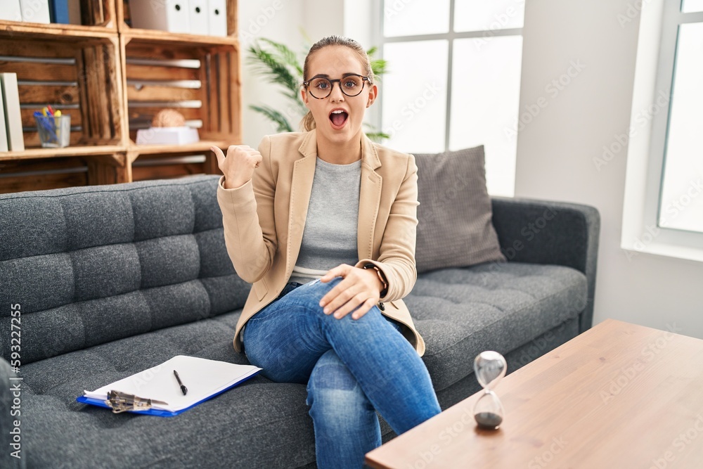 Young woman working at consultation office surprised pointing with hand finger to the side, open mouth amazed expression. Young woman working at consultation office surprised pointing with hand finger to the side, open mouth amazed expression.