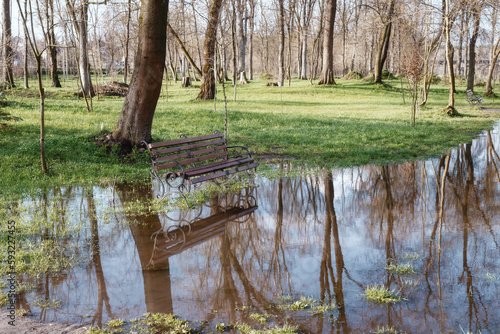 A bench near a large puddle of water. In the park after the rain. Lots of water after rain in the park on a rainy day.