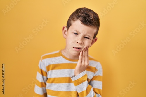 Young caucasian kid standing over yellow background touching mouth with hand with painful expression because of toothache or dental illness on teeth. dentist