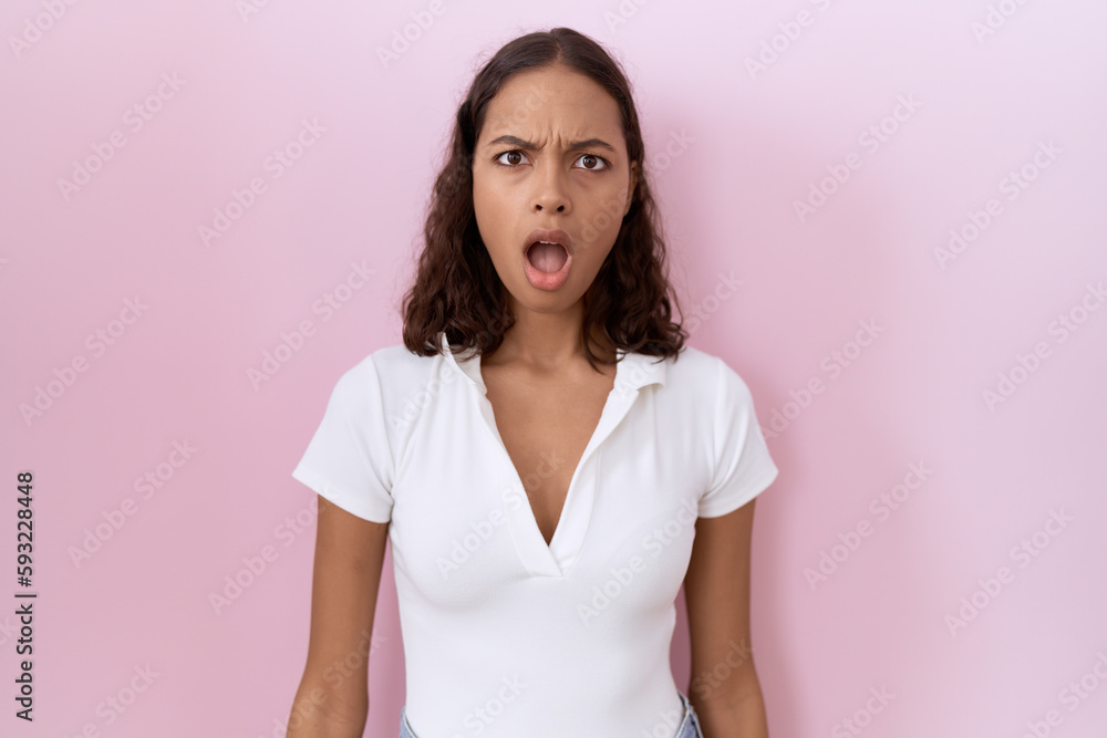 Young hispanic woman wearing casual white t shirt in shock face, looking skeptical and sarcastic, surprised with open mouth Young hispanic woman wearing casual white t shirt in shock face, looking skeptical and sarcastic, surprised with open mouth