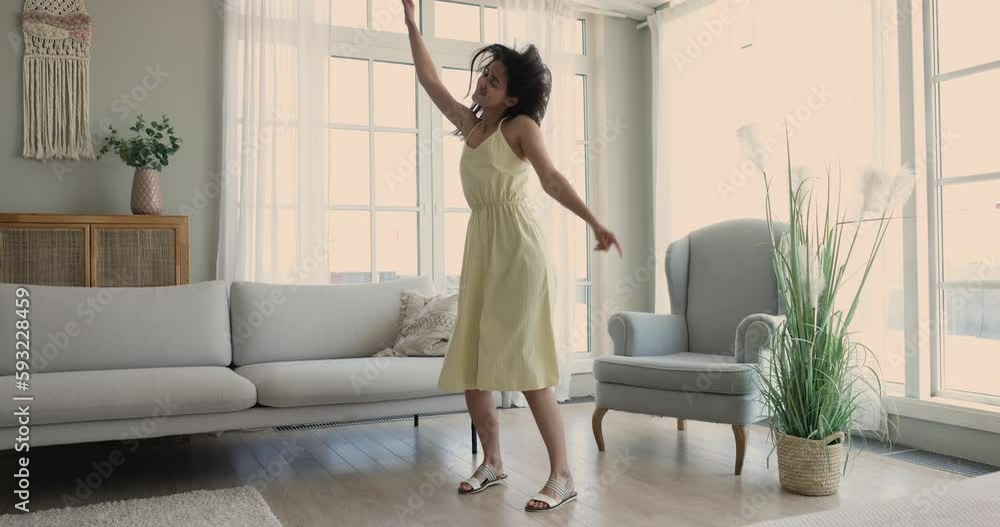 Happy excited late teen girl in summer dress dancing to music in modern living room with large window, smiling with closed eyes, enjoying ,movement, motion at home. Full length Happy excited late teen girl in summer dress dancing to music in modern living room with large window, smiling with closed eyes, enjoying ,movement, motion at home. Full length