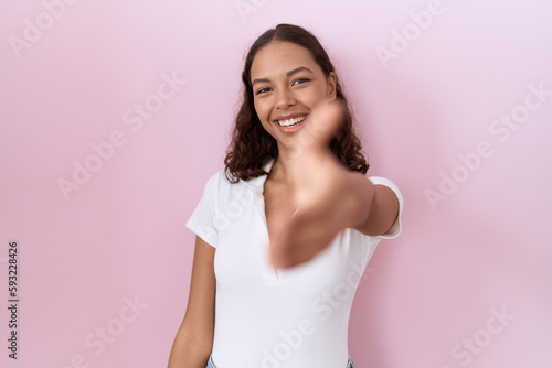 Young hispanic woman wearing casual white t shirt smiling friendly offering handshake as greeting and welcoming. successful business.