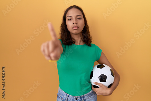 Young hispanic woman holding ball pointing with finger up and angry expression, showing no gesture © Krakenimages.com