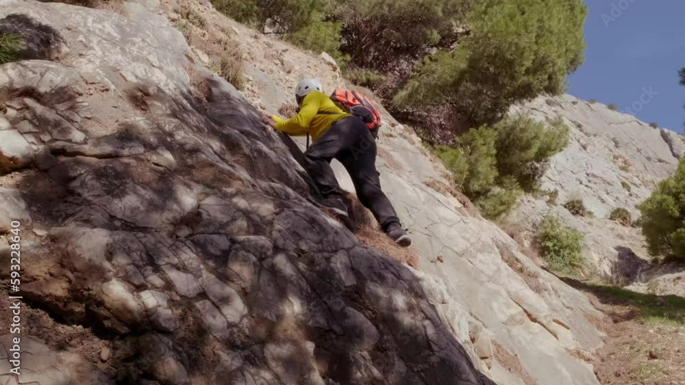 tourist in yellow jacket with orange backpack on back climbs cliff, mature man in safety helmet, rock climber, extreme lifestyle of people, mountaineering, life insurance, extreme sports tourist in yellow jacket with orange backpack on back climbs cliff, mature man in safety helmet, rock climber, extreme lifestyle of people, mountaineering, life insurance, extreme sports
