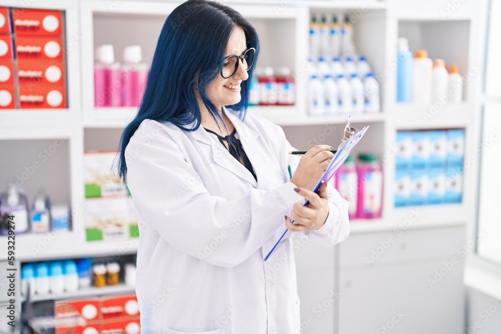 Young caucasian woman pharmacist smiling confident writing on document at pharmacy