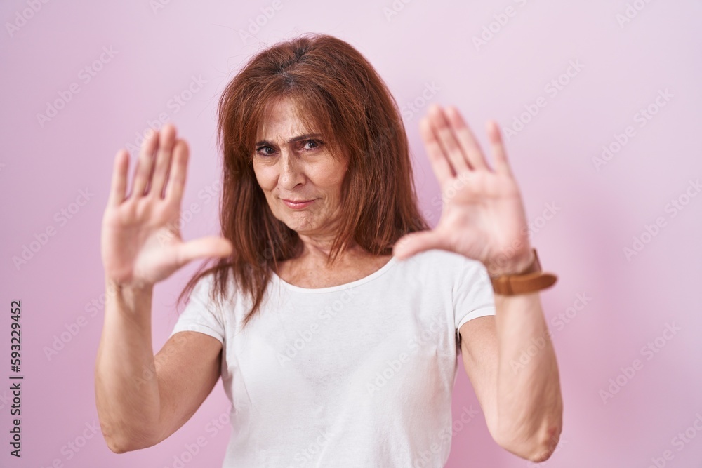 Middle age woman standing over pink background doing frame using hands palms and fingers, camera perspective Middle age woman standing over pink background doing frame using hands palms and fingers, camera perspective