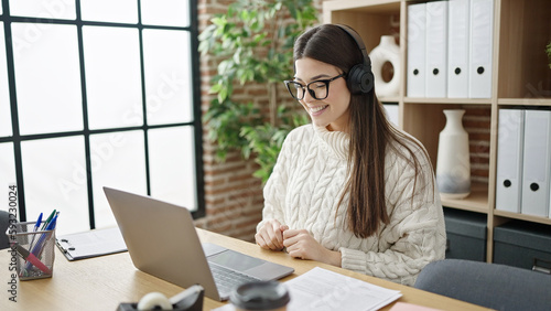 Young beautiful hispanic woman business worker using laptop and headphones working at office